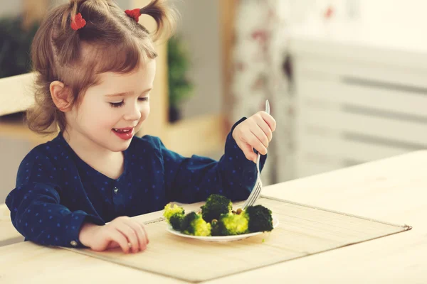 Happy child girl  eating vegetables and laughs — Stock Photo, Image