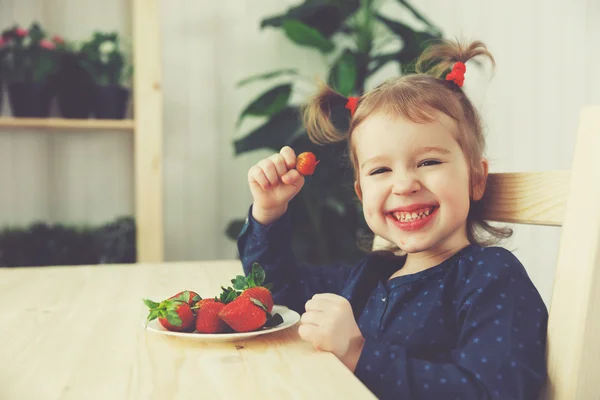 Щаслива дитина дівчина їсть полуницю на літній домашній кухні — стокове фото