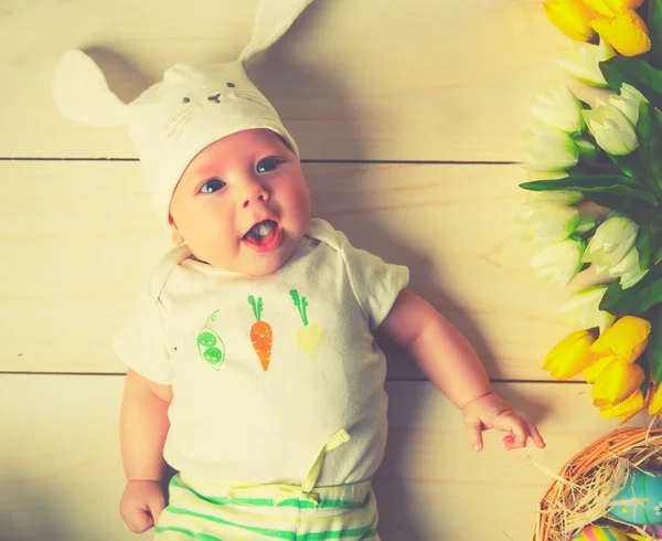 Niño feliz bebé con orejas de conejo de Pascua y flores — Foto de Stock