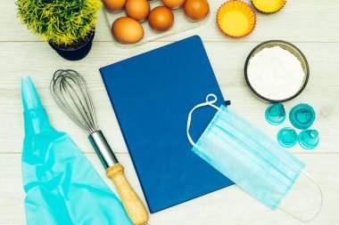 Kapalı tarif kitabı, yumurta ve un, ahşap masada tıbbi maske.