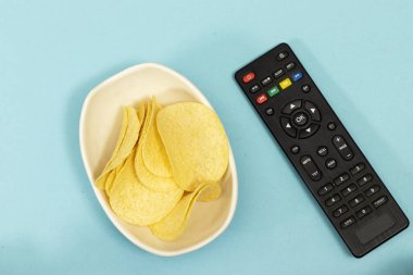 Çıtır patates cipsi ve mavi arka planda uzaktan kumanda.