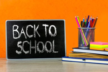 Okul konseptine geri dönelim. Kalem kutusu, kitap, defter ve tahta üzerine yapışkan bir not.