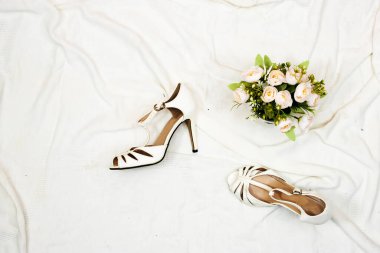 Gelin ayakkabıları ve bir buket çiçek. Yatakta düğün konsepti 