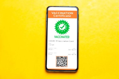 Sarı arka planda cep telefonunda dijital aşı sertifikası. Bu uygulama Coronavirus covid-19 aşısı olduğunu doğrulamak için.