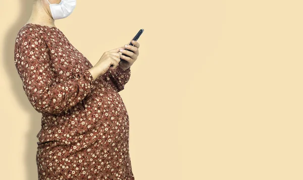 Álló Terhes Orvosi Maszkot Visel Mobiltelefont Használ Otthon Terhesség Technológia — Stock Fotó