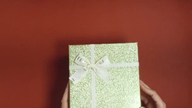 Kırmızı arka planda elleri ile tutulan beyaz kurdeleli altın hediye kutusu kutlama için.