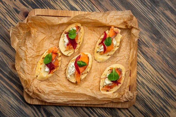 Toasts with red fish and greens on food paper on a wooden background — Stock Photo, Image