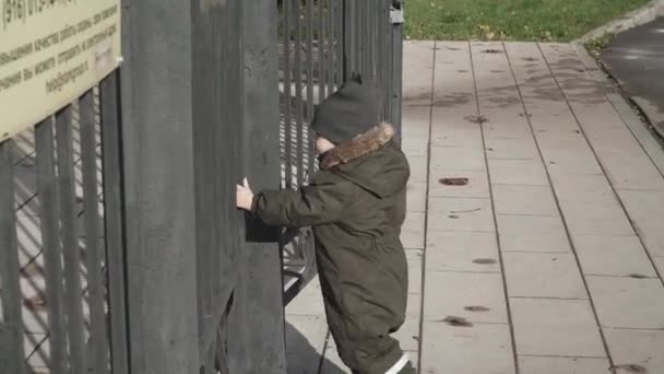 Мальчик закрывает высокие железные ворота — стоковое видео