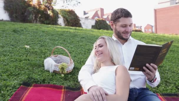 Pareja en el césped libro de lectura y sonrisa — Vídeo de stock