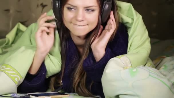 Дівчина з навушниками посміхається ліжко додому — стокове відео
