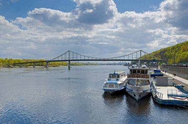 Footbridge Dnipro nehri, mavi gökyüzünün altında Kyiv Ukrayna 'nın turist tekneleriyle dolup taşıyor.