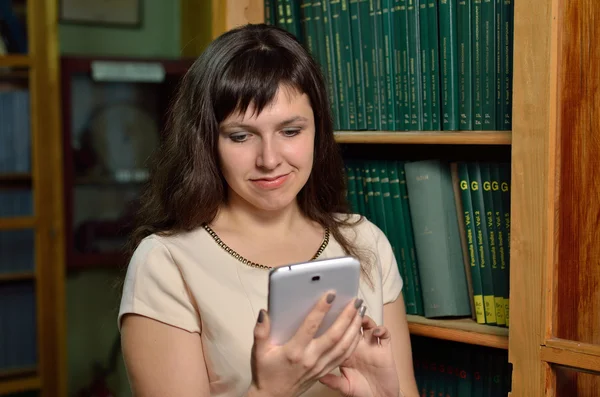 Young woman with a gadget in the library — Stock Photo, Image