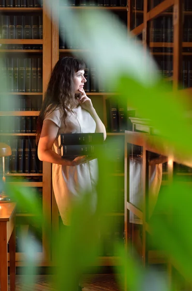 A pensive woman with the books through the green leaves — Stock Photo, Image