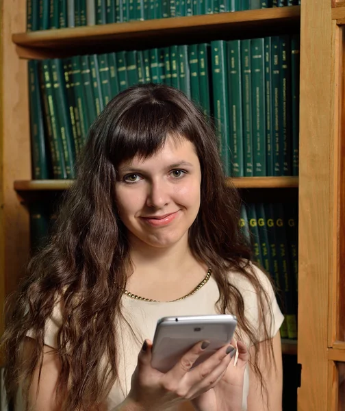 Eine Frau mit einem Gerät gegen den Büchertisch — Stockfoto