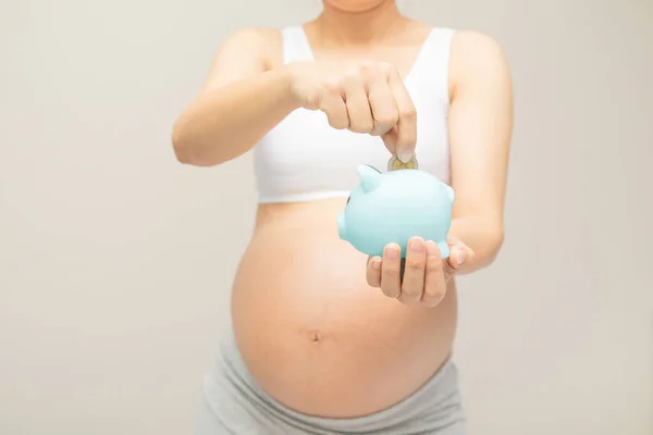 Para tasarrufu, bağış, ekonomi, hamilelik, rezervasyon, finans, yatırım ve hayat sigortası konsepti. Para biriktirmek için kumbaraya altın para atan genç ve güzel hamile kadın.