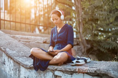 Tablet kullanan ve kulaklık takan konsantre bir kadın. Parkta hoş bir yürüyüş. Sokak tarzı, şehir yürüyüşü ve müzik fikri