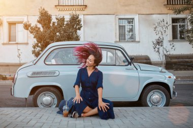 Yeni duygular, şehir yürüyüşü ve sokak tarzı konsept. Mutlu kadın mavi arabanın yanında eğleniyor. Parlak pembe saçlı kadın..