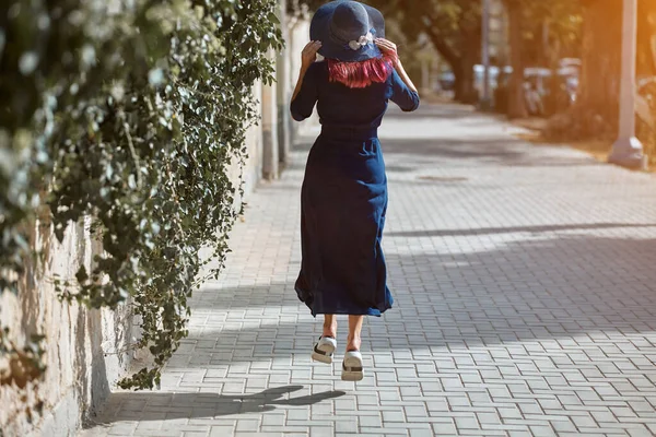 Kobieta skacząca po drodze. Słońce pada na asfalt. Szczęśliwa dama w niebieskiej sukience. Ulica styl i czas wolny pomysł — Zdjęcie stockowe