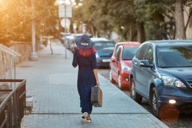 Bavul ve şapkayla caddede yürüyen şık bir kadın. Önümüzde uzun bir yol ve arabalar var. Seyahat zamanı ve yeni yerler kavramı