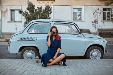 Yeni duygular, yeni bir yer ve yolculuk konsepti. Elinde fotoğraf makinesi olan genç ve güzel bir bayan. Bayan arabanın yanında oturuyor.