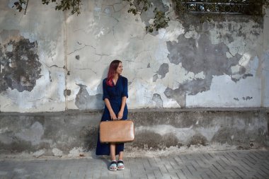 Seyahat zamanı, yeni duygular ve yeni yer konsepti. Elinde bavulla gülümseyen güzel kadın. Eski duvar arkasında poz veren kadın.