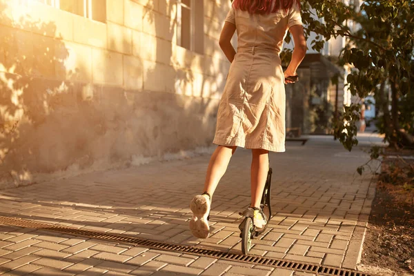 Dziewczyna w sukience jeżdżąca na skuterze na ulicy. Zachód słońca pada na zewnątrz. Nowe emocje i czas wolny pomysł, przestrzeń kopiowania — Zdjęcie stockowe
