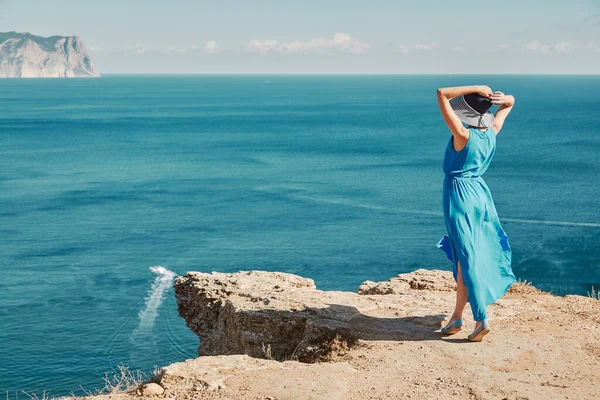 Temps de trajet et nouvelle idée de terrain. Femme en robe bleue et chapeau bénéficiant d'une vue sur l'océan depuis la montagne. Bateau flottant en mer. — Photo