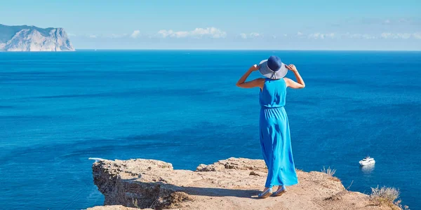 Dama de vestido y sombrero posando en la cima del acantilado. Vistas al mar y aire fresco. Tiempo de viaje y viaje al extranjero concepto, espacio de copia —  Fotos de Stock