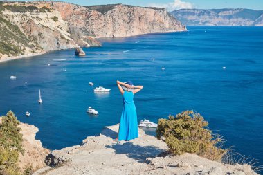 Güzel sahil şeridini izleyen bir kadın. Denizde yüzen yatlar ve muhteşem dağlar. Seyahat ve tatil kavramı