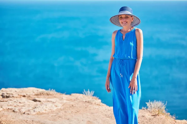 Lächelnde glückliche Frau posiert im blauen Kleid mit Ozean auf dem Hintergrund. Erholungsurlaub und Tourismuskonzept, Kopierraum — Stockfoto