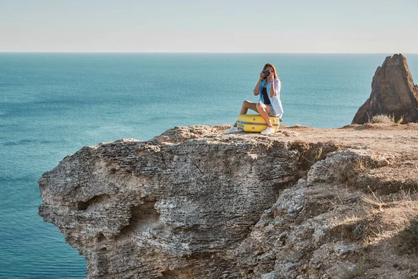 Tiempo de viaje nuevo concepto de tierra y oficina remota, espacio de copia. Señora sentada en una maleta amarilla tomando fotos de la naturaleza. —  Fotos de Stock