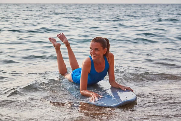 Woman learning to surf on summer vacation. Happy cute girl sitting on sand in ocean. Adventure time and beach concept