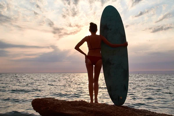 Summer vacation, beach time and adventure concept. Woman on rock with board for surfing waving with hand. Copy space — Stock Photo, Image