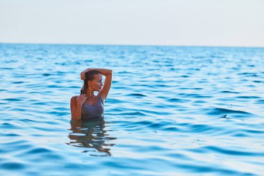 Mavi deniz suyunda poz veren çekici bir kadın. Seksi kadın mutluluktan başka tarafa bakıyor. Yaz tatili ve tatil fikri