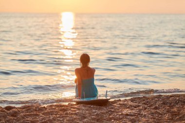 Sahilde gün batımını izleyen bir bayan. Kız sakin bir atmosferde dinleniyor. Dinlenme ve tatil gezisi için zaman fikri, boşluğu kopyala