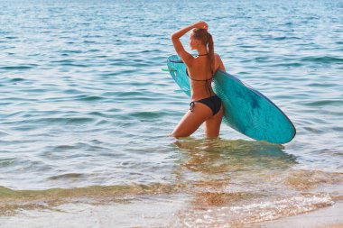 Kumlu deniz kıyısında güneşli bir gün. Sörf tahtası olan formalı bir kız. Yaz zamanı, sörf sporu fikri. Macera gezisi konsepti