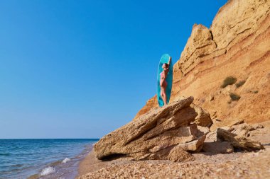 Uçurumda güneşlenen bir kadın, sahilde sıcak bir yaz günü. Yaz zamanı, plaj günü, tatil gezisi, sörf fikri, fotokopi alanı