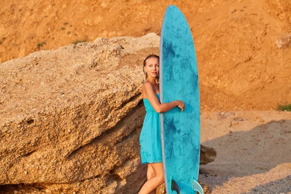 Summer time and surf sport idea. Adventure time concept. Cute girl looking out blue surfboard. Woman relaxing on trip.