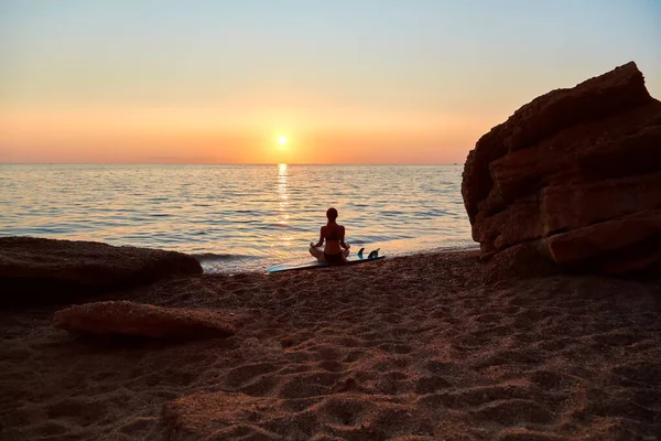 Девушка медитирует в спокойный закатный вечер сидеть на песке. Идея летнего времени и времени, чтобы расслабиться. Желание приключений Стоковая Картинка