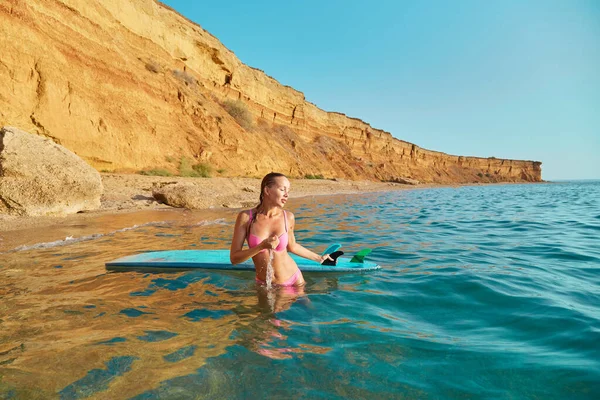 Красива дівчина в морській воді з дошкою для серфінгу. Вид на гори на тлі. Літній час, відпустка та спортивна ідея серфінгу — стокове фото