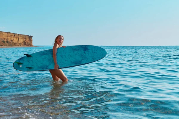 Щаслива дівчина гуляє в океані з дошкою для серфінгу. Спокійний вид на море в літній день. Ідея серфінгу, пляжний день і літній відпочинок — стокове фото