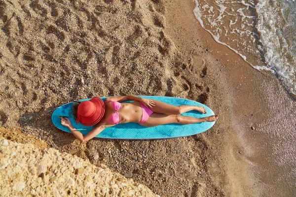 Femme allongée sur planche de surf sur plage de sable couverture visage avec chapeau. Heure d'été, surf et temps de voyage, envie d'aventure Photos De Stock Libres De Droits