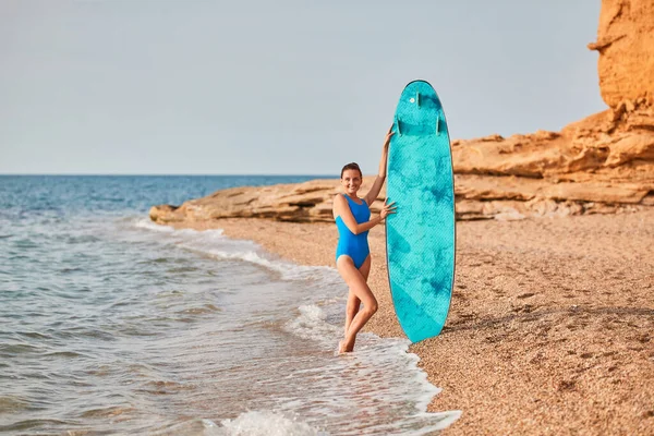 Пані в купальнику з дошкою для серфінгу. Серф-хобі, літні канікули та пригодницька ідея. Вид на океан і піщаний пляж. Копіювати простір — стокове фото