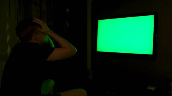 Πλευρική άποψη ενός συναισθηματικού ανθρώπου βλέποντας τηλεόραση με πράσινη οθόνη στο σπίτι το βράδυ. Έννοια. Άνθρωπος που αναζητούν τόνισε και απογοητευμένος, ενώ βλέποντας αθλητικό παιχνίδι στην τηλεόραση με chroma κλειδί. — Φωτογραφία Αρχείου