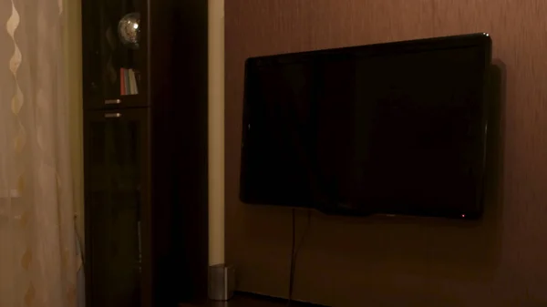 大規模なテレビをオフにリビングルームのインテリアの詳細。コンセプト。狭い木製の秘書の近くの茶色の壁にかかっているフラットLCDテレビ. — ストック写真