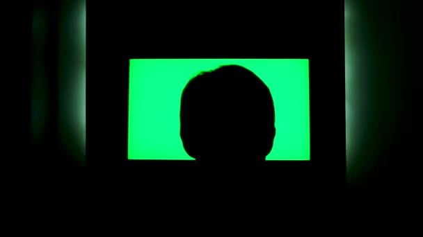 Vista trasera de una silueta de cabeza masculina delante de la televisión con pantalla verde. Concepto. Hombre viendo la televisión con chromakey que cuelga en el wll por la noche en casa. — Vídeos de Stock