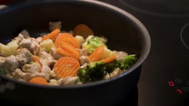 Cooking chicken with vegetables in a black frying pan standing on a touch sensitive hob. Concept. Preparing healthy dinner, frying carrots, broccoli, and cauliflower with white chicken meat. — Stock Footage Cooking chicken with vegetables in a black frying pan standing on a touch sensitive hob. Concept. Preparing healthy dinner, frying carrots, broccoli, and cauliflower with white chicken meat. Stock Footage