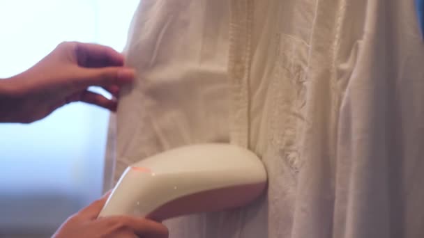 Frau bügelt Hemd mit Dampfbügeleisen. Konzept. Großaufnahme einer Mädchenhände, die Dampfgarer benutzt, um zu Hause weißes Hemd gegen das Fenster zu bügeln.