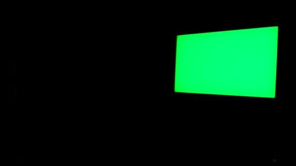 Pantalla verde aislada sobre fondo negro. Concepto. TV con llave croma brillante colgando en la pared negra de la habitación por la noche. — Vídeo de stock