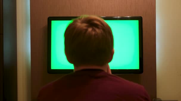 Kanepede oturan, yeşil ekranlı büyük düz ekran TV izleyen genç bir adamın arka görüntüsü. Kavram. Erkek evde, krom anahtarla TV karşısında dinleniyor.. — Stok video